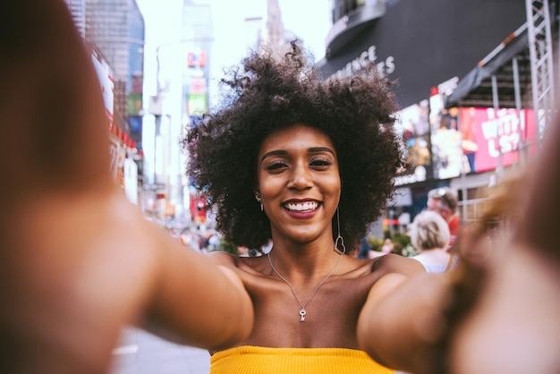 Portret szczęśliwej młodej kobiety z fryzurą afro robiącej selfie na ulicy