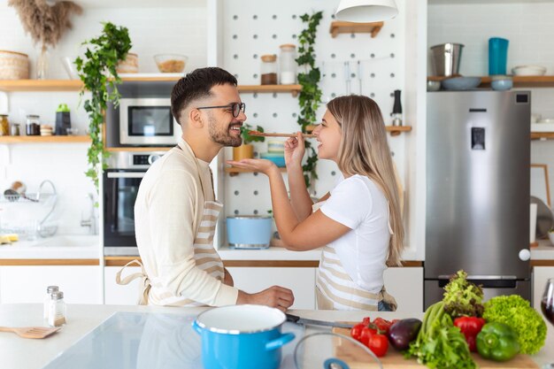 Portret szczęśliwej młodej pary gotującej razem w kuchni w domu romantyczna atrakcyjna młoda kobieta i przystojniak cieszą się wspólnym spędzeniem czasu, stojąc na świeconej nowoczesnej kuchni