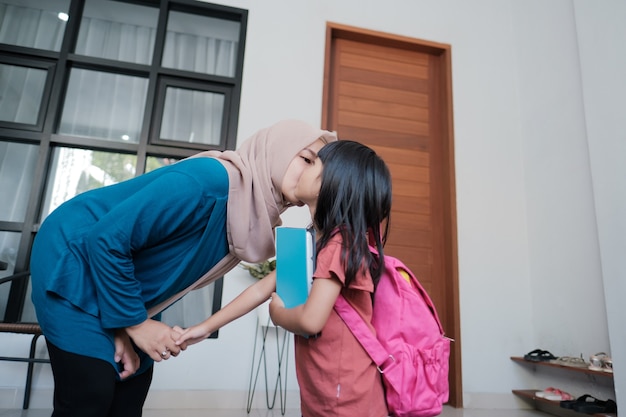 Portret szczęśliwej muzułmańskiej matki całuje jej policzek dziecka rano w domu przed dniem szkolnym