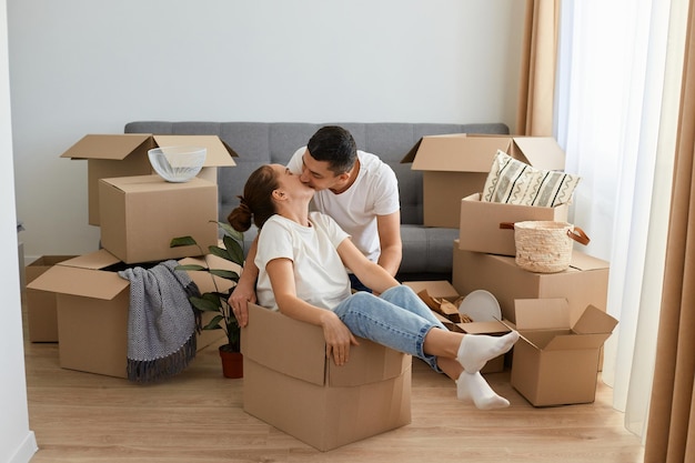 Portret szczęśliwej pary romantycznej bawiącej się podczas przeprowadzki do nowego domu atrakcyjna kobieta siedzi w kartonowym pudełku, podczas gdy mężczyzna całuje ją z miłością na delikatną
