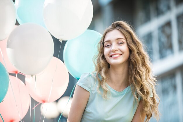 Portret szczęśliwej pięknej kobiety z latającymi wielokolorowymi balonami w mieście