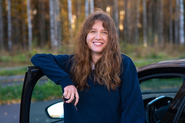 Portret szczęśliwej pozytywnej dziewczyny młoda kobieta kierowca siedzi w swoim samochodzie nowym samochodem, ciesząc się jazdą i śmiejąc się Radosna dama w samochodzie patrząca na kamerę stojącą w pobliżu samochodu trzymająca klucze
