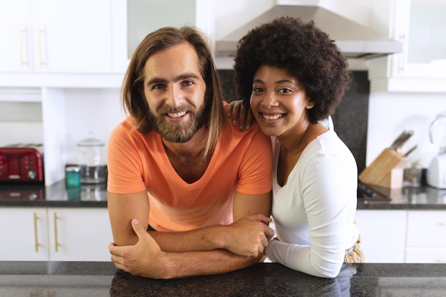 Portret szczęśliwej, różnorodnej pary w kuchni, uśmiechając się i obejmując
