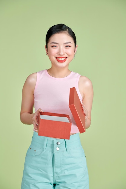 Portret szczęśliwej uśmiechniętej dziewczyny otwierającej pudełko prezenta odizolowane na zielonym tle