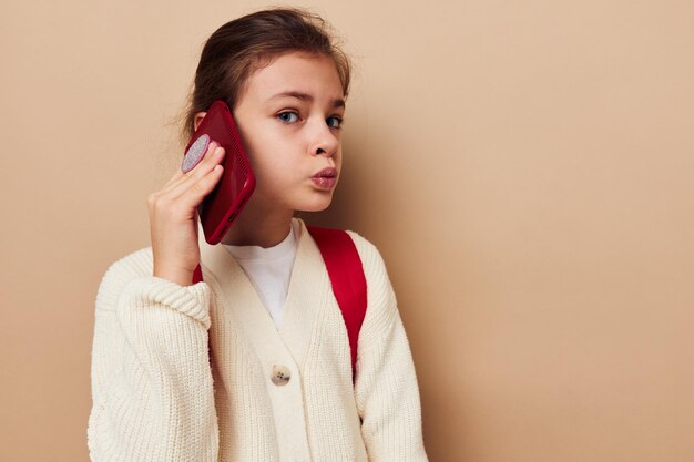 Portret szczęśliwej uśmiechniętej dziewczyny rozmawiającej przez telefon z beżowym tłem plecaka