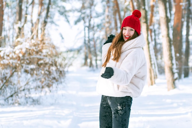 Portret szczęśliwej uśmiechniętej dziewczyny w zimowym lesie Kaukaska kobieta w czerwonym kapeluszu z dymienicą w śnieżnym parku Portret w ruchu