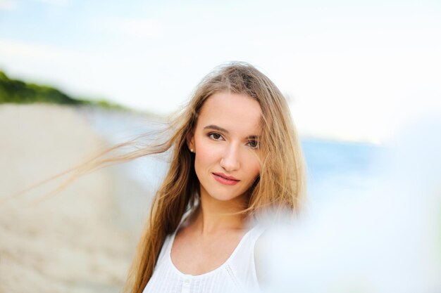 Portret szczęśliwej uśmiechniętej kobiety w wolnym szczęściu, błogosławieństwie na plaży oceanu, cieszącej się naturą podczas podróży, wakacji na świeżym powietrzu, widok przez białe rozmyte kwiaty