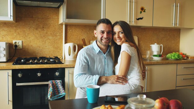 Portret szczęśliwej uśmiechniętej pary siedzącej w kuchni wczesnym rankiem w domu