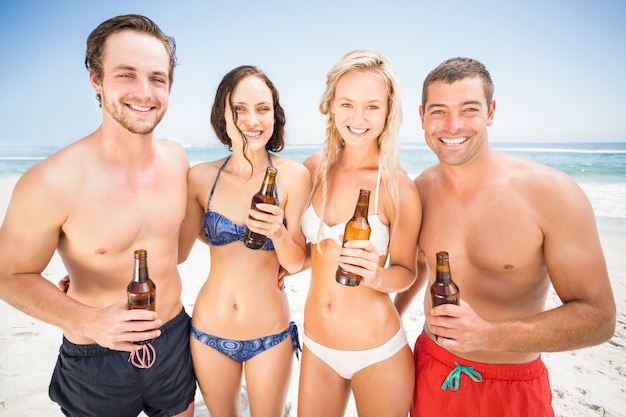 Portret szczęśliwi przyjaciele stoi na plaży z piwnymi butelkami