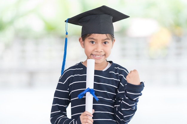 Portret szczęśliwy azjatyckie dziecko absolwentka szkoły żeńskiej w kasztana posiada walcowane świadectwo. Graduation Celebration Concept Stock Photo