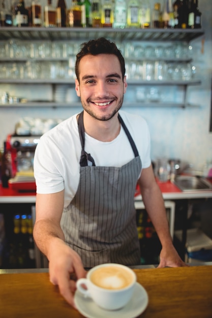 Portret szczęśliwy barista oferuje kawę przy bufetem