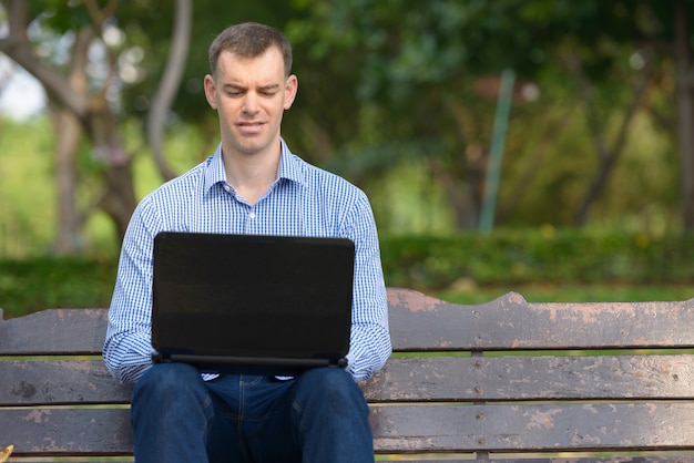 Portret szczęśliwy biznesmen za pomocą laptopa w parku