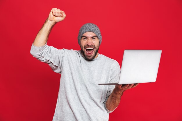 Portret szczęśliwy facet 30s w casual nosić radość trzymając srebrny laptop na białym tle