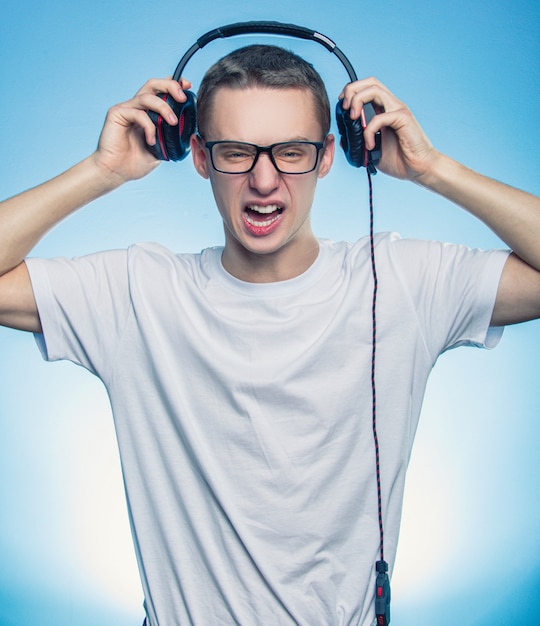 Portret szczęśliwy krzyczący mężczyzna słuchania muzyki w słuchawkach i usunął je z głowy na niebieskim tle.