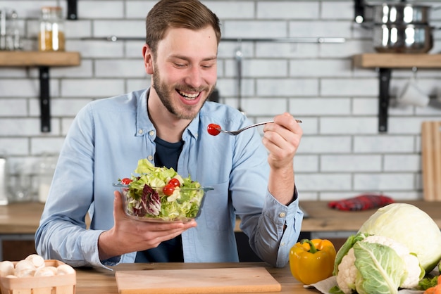 Zdjęcie portret szczęśliwy mężczyzna je świeżej sałatki w kuchni