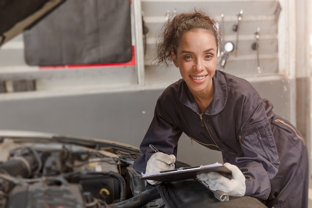 Portret szczęśliwy pracownik African American kobieta pracy dla mechanika samochodowego w garażu sprawdzania silnika samochodu.