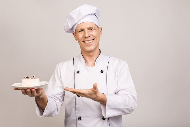 Portret szczęśliwy starszy mężczyzna kucharz ubrany w jednolity talerz gospodarstwa z kawałkiem ciasta