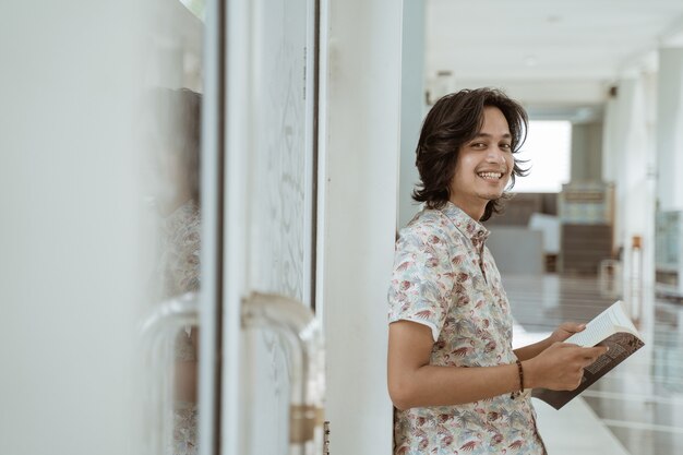 Portret szczęśliwy studentka trzymając książkę i patrząc na kamery w kampusie.