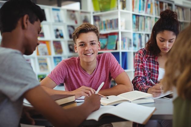 Portret szczęśliwy uczeń studiuje z kolegami z klasy w bibliotece