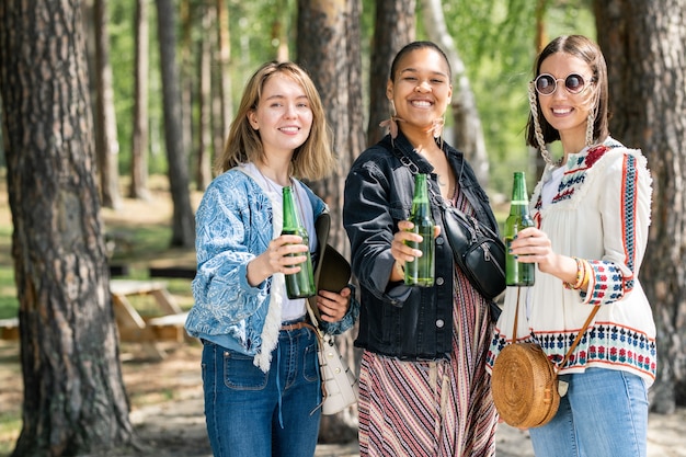 Portret szczęśliwych młodych wieloetnicznych dziewcząt razem picia piwa na kempingu w lesie