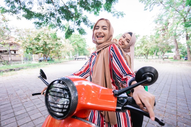 Portret szczęśliwych muzułmańskich dziewcząt jeżdżących skuterem cieszyć się letnimi wakacjami z przyjaciółmi