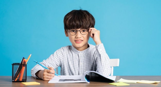 Portret szkolnego chłopca siedzącego i studiującego na niebieskim tle