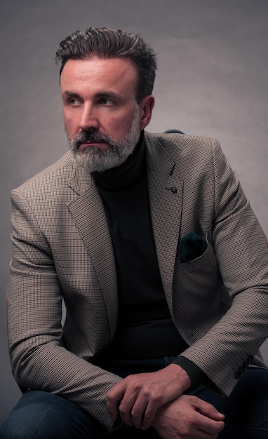 Portret udanego, stylowego, eleganckiego, starszego biznesmena z siwą brodą i dorywczo ubraniem biznesowym pewny siebie w studio fotograficznym na białym tle na ciemnym tle, gestykulując rękami. Zdjęcie wysokiej jakości