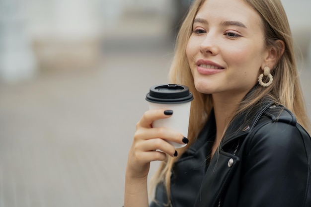 Portret ufnej szczęśliwej młodej kobiety blondynki pije kawę z białej papierowej filiżanki