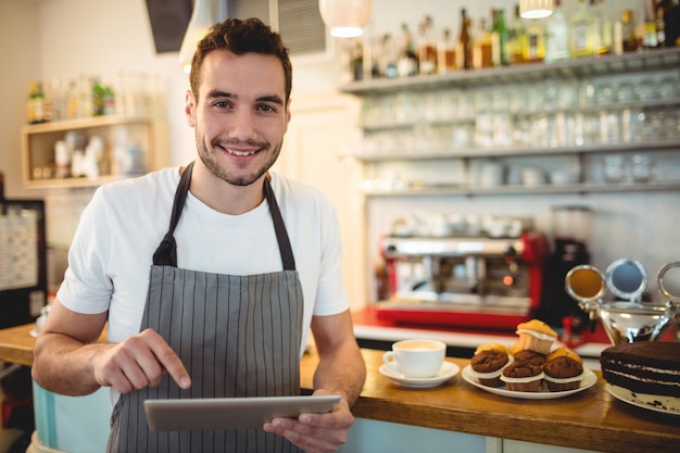 Portret ufny barista używa cyfrową pastylkę przy kawiarnią