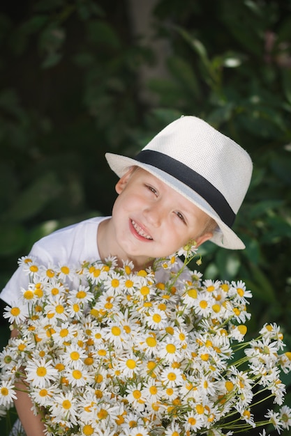 Portret urocza chłopiec w kapeluszu z dużym białym bukietem rumianki