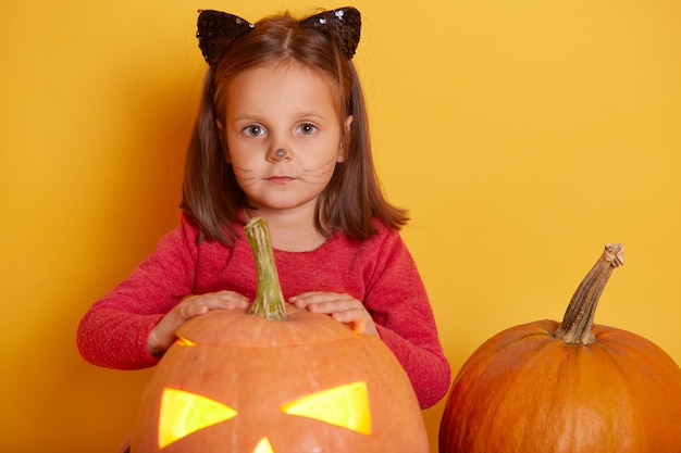 Portret Urocza śmieszna Kaukaska Mała Dziewczynka Ubierał Czerwoną Koszula Z Pomarańczową Halloweenową Banią. Dzieci Bawiące Się, Zabawy W Studio Na Jesień Sezonowe Wakacje. Dzieciak Pozuje Blisko Dyniowego Jack O Lantern.