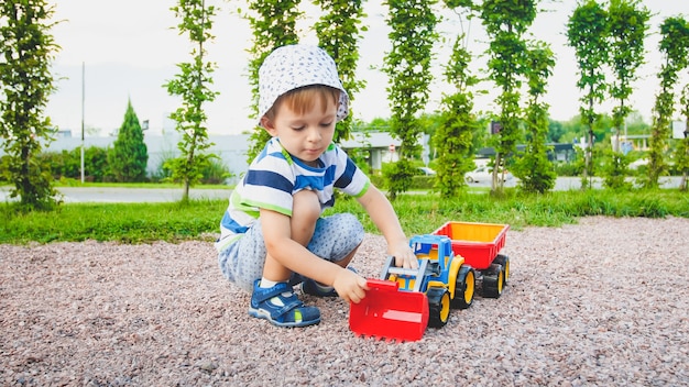 Portret Uroczego 3-letniego Chłopca Bawiącego Się Zabawkową Ciężarówką Z Przyczepą Na Placu Zabaw W Parku