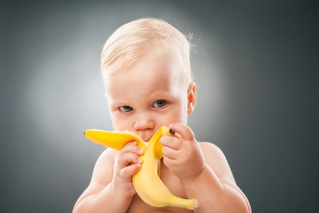 Portret uroczego dziecka jedzącego banana na szarym tle