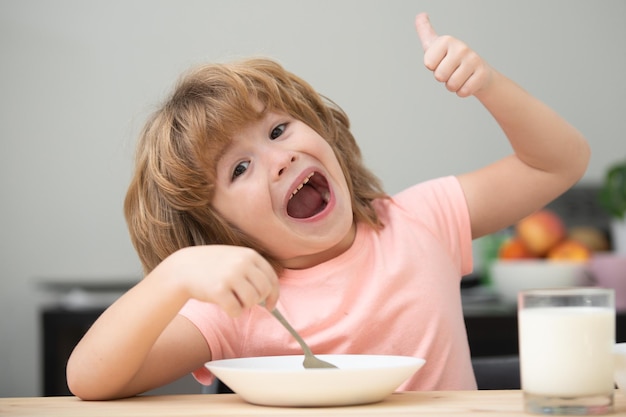 Portret uroczego dziecka jedzącego zupę lub śniadanie jedzące obiad przy stole w domu z łyżką ki