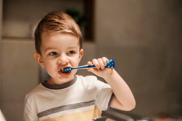 Portret uroczego małego chłopca stojącego przed lustrem i myjącego zęby