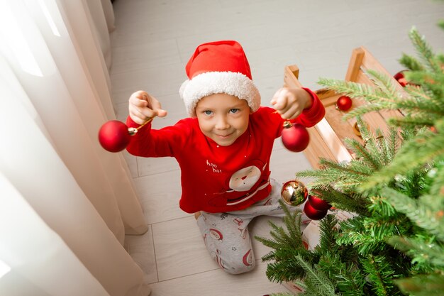 portret uroczego małego chłopca w czerwonej piżamie dekorującej choinkę zimową koncepcję nowego roku