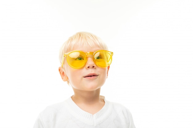 portret uroczego uśmiechniętego blond chłopca w okularach przeciwsłonecznych ubranego w białą koszulkę na białym