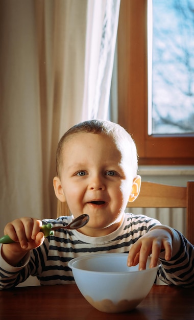 Portret uroczego uśmiechniętego chłopca jedzącego jedzenie w domu