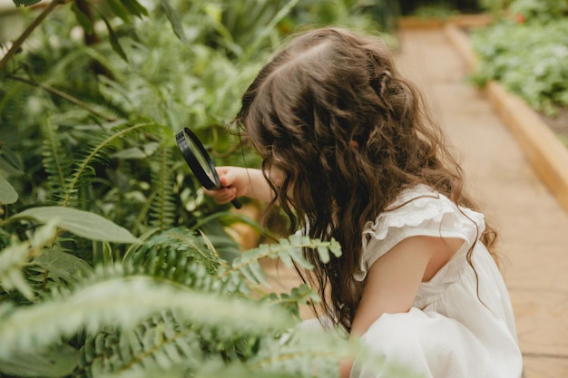 Portret uroczej dziewczynki patrzącej na rośliny przez szkło powiększające Dziecko z lupą bada przyrodę w ogrodzie Koncepcja wczesnego rozwoju