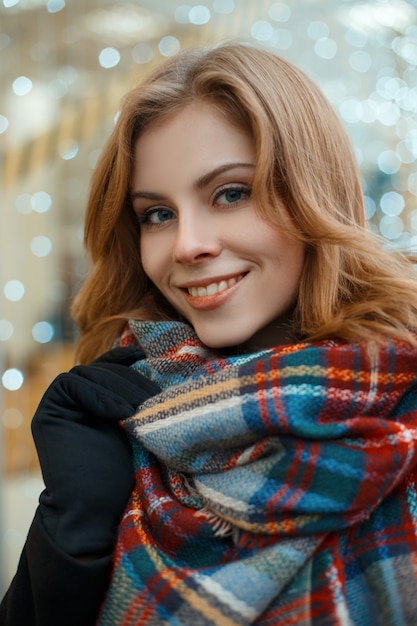 Portret uroczej kobiety o blond włosach i pięknym uśmiechu w czarnym stylowym płaszczu w czarnych rękawiczkach z wełnianym ciepłym szalikiem