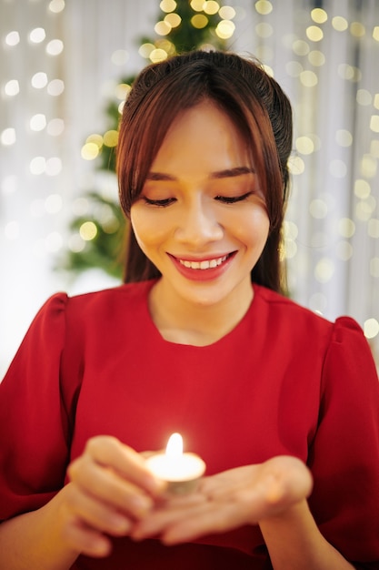 Portret uroczej młodej kobiety patrzącej na małą płonącą świeczkę w dłoni