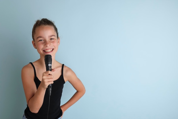 Portret uroczej nastolatki śpiewającej za pomocą mikrofonu Nastolatka w czarnej koszulce na odizolowanym niebieskim tle Karaoke dla dzieci domowa rozrywka dla dzieci Piosenkarka śpiewa z mikrofonem