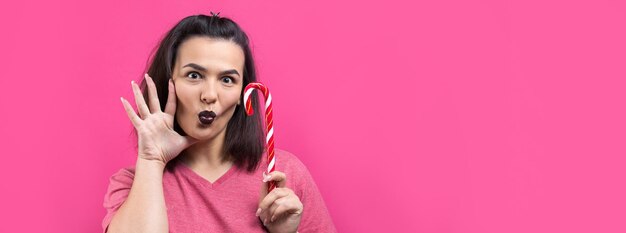 Portret uroczej, słodkiej, pięknej, wesołej kobiety z prostymi brązowymi włosami, próbującej ugryźć Boże Narodzenie z czerwonej trzciny cukrowej