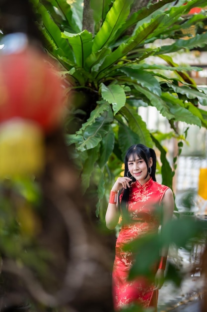 Portret uśmiecha się Azjatka transpłciowa kobieta ubrana w czerwoną sukienkę cheongsam tradycyjną dekorację na festiwal chińskiego nowego roku świętuje kulturę Chin w chińskiej świątyni Miejsca publiczne w Tajlandii