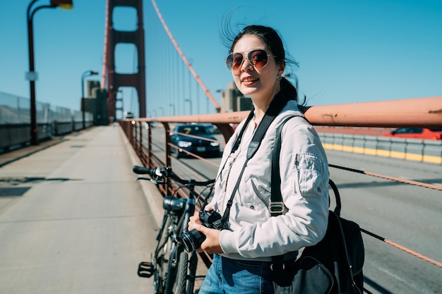 portret uśmiechnięta azjatycka fotografka patrzy w dal, opierając się o balustradę mostu złotej bramy w San Francisco w Kalifornii