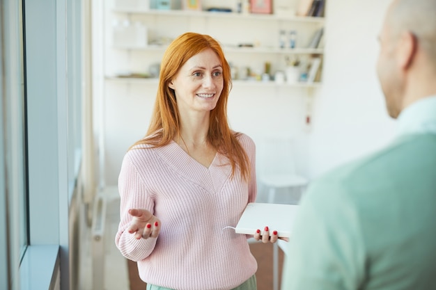 Portret uśmiechnięta bizneswoman mówi do dojrzałego mężczyzny stojąc w nowoczesnym biurze, kopia przestrzeń