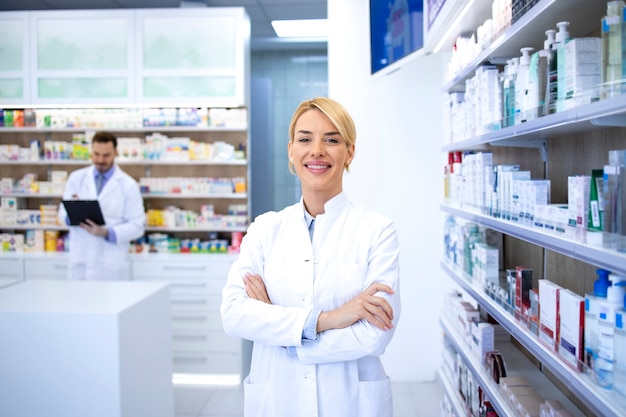 Portret uśmiechnięta blondynka farmaceuta stojąca w aptece lub drogerii z rękami skrzyżowanymi.