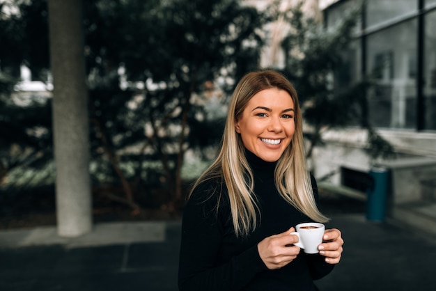 Portret uśmiechnięta blondynki kobieta trzyma filiżankę kawy. Patrząc na aparat.