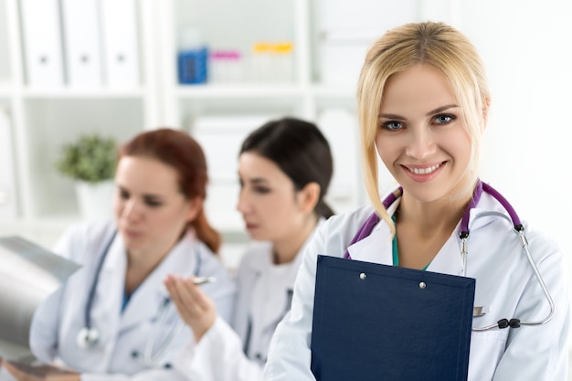 Zdjęcie portret uśmiechnięta kobieta lekarz medycyny gospodarstwa niebieski folder dokumentów z dwoma kolegami patrząc na zdjęcie rentgenowskie. koncepcja opieki zdrowotnej i medycyny.