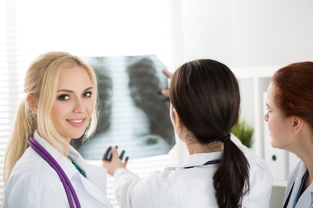 Portret uśmiechnięta kobieta lekarz medycyny z dwoma kolegami patrząc na zdjęcie rentgenowskie. Koncepcja opieki zdrowotnej i medycyny.
